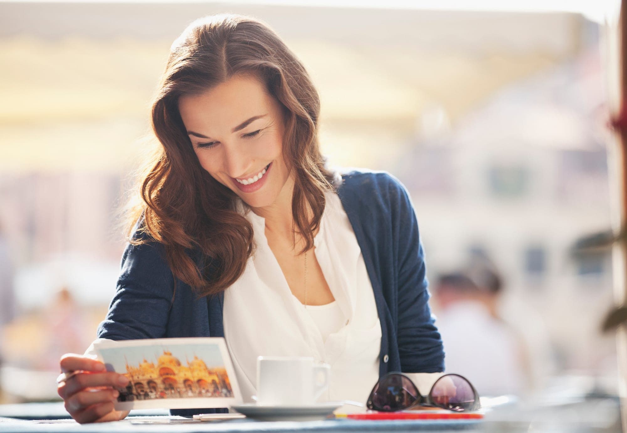 Smiling woman reading a handwritten postcard at a sidewalk café