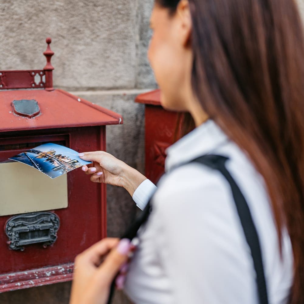 A woman posting a picture postcard into an old red postbox