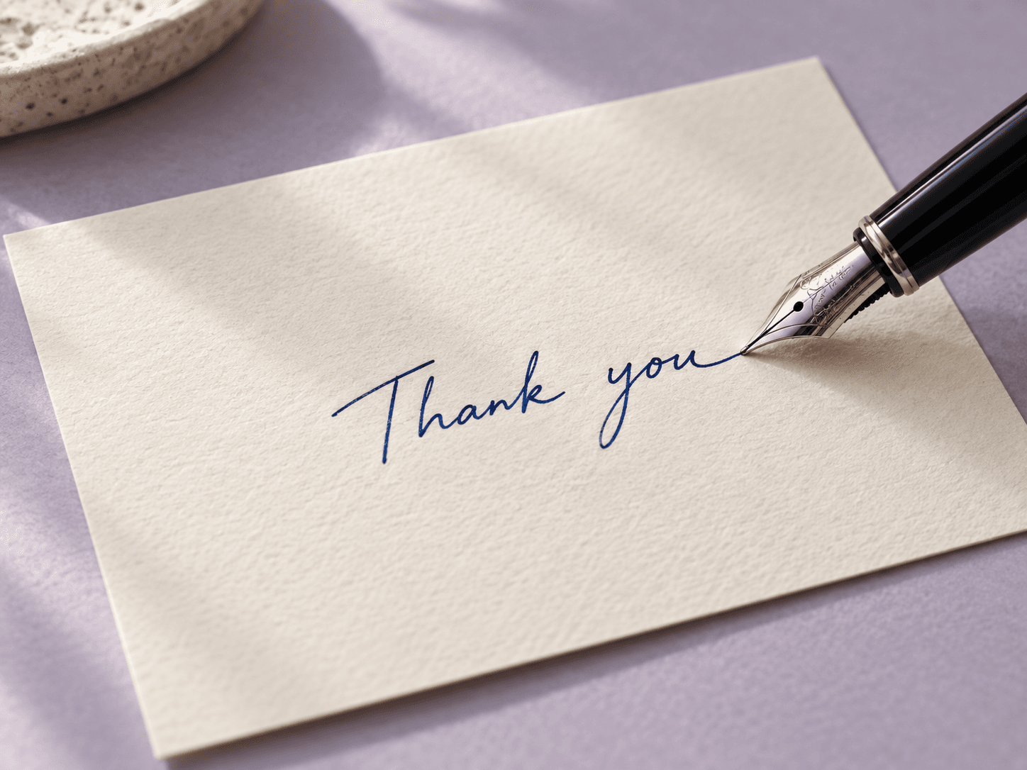 Fountain pen nib touching blue Thank you lettering on textured cardstock