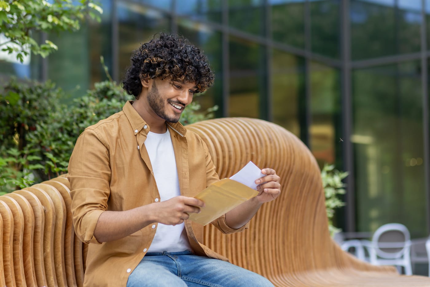 A smiling young man on a bench outside, reading a card he has just taken from its envelope