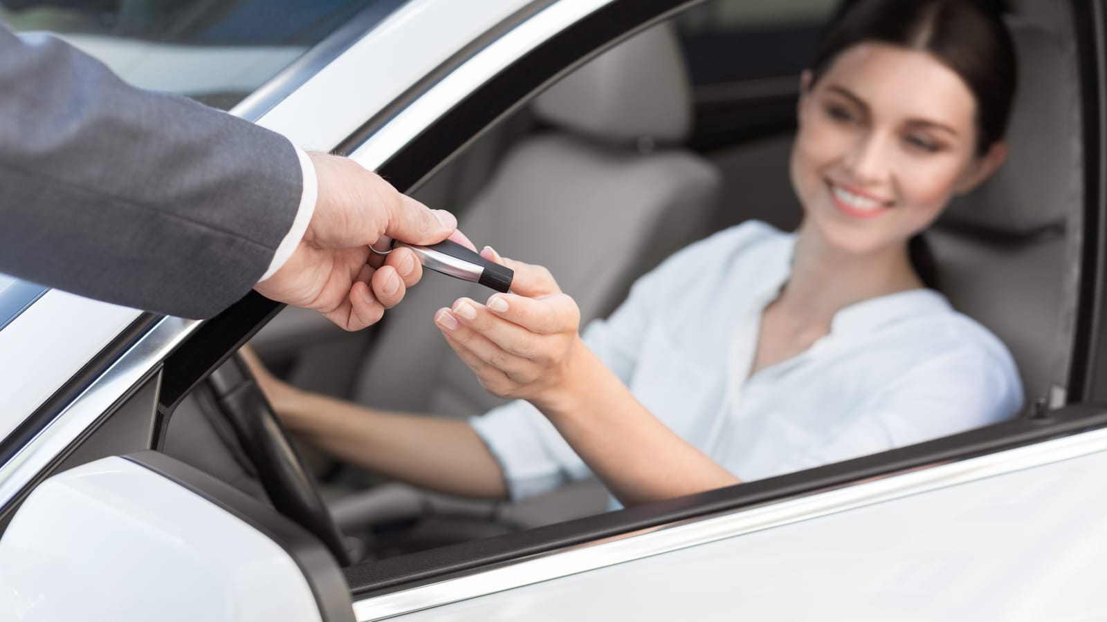 A car salesperson at a dealership desk writing a thank-you card by hand, a new car key fob resting beside the envelope
