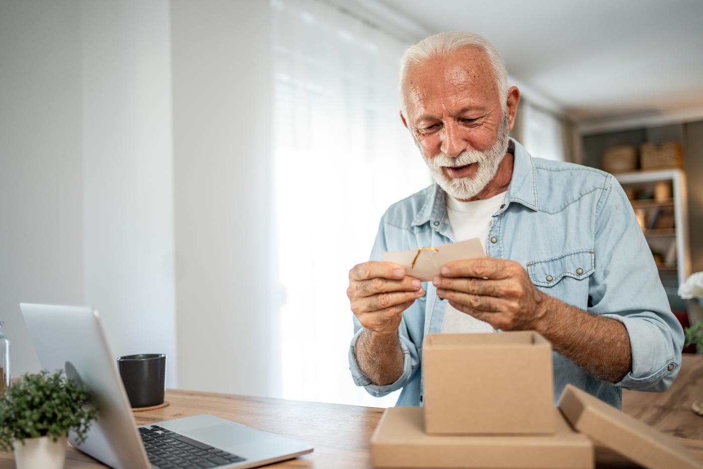 A smiling older man at home unboxing a parcel and reading the greeting card that came in it