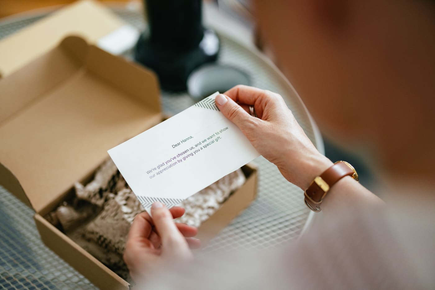 A woman holding a short personal thank-you note she has lifted out of an open cardboard gift box