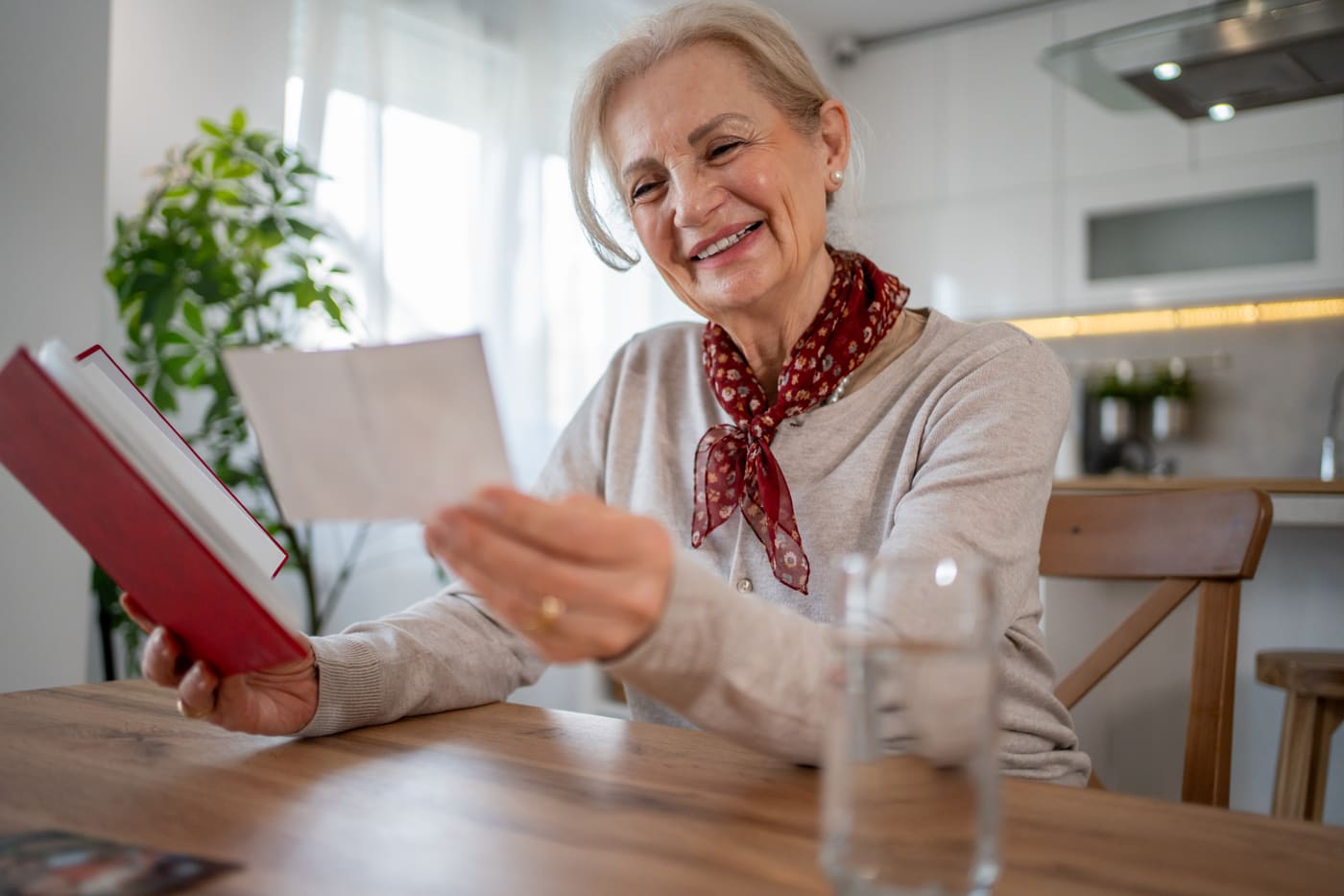 A woman at her kitchen table smiling as she reads a handwritten card from a charity, the envelope open beside her mug