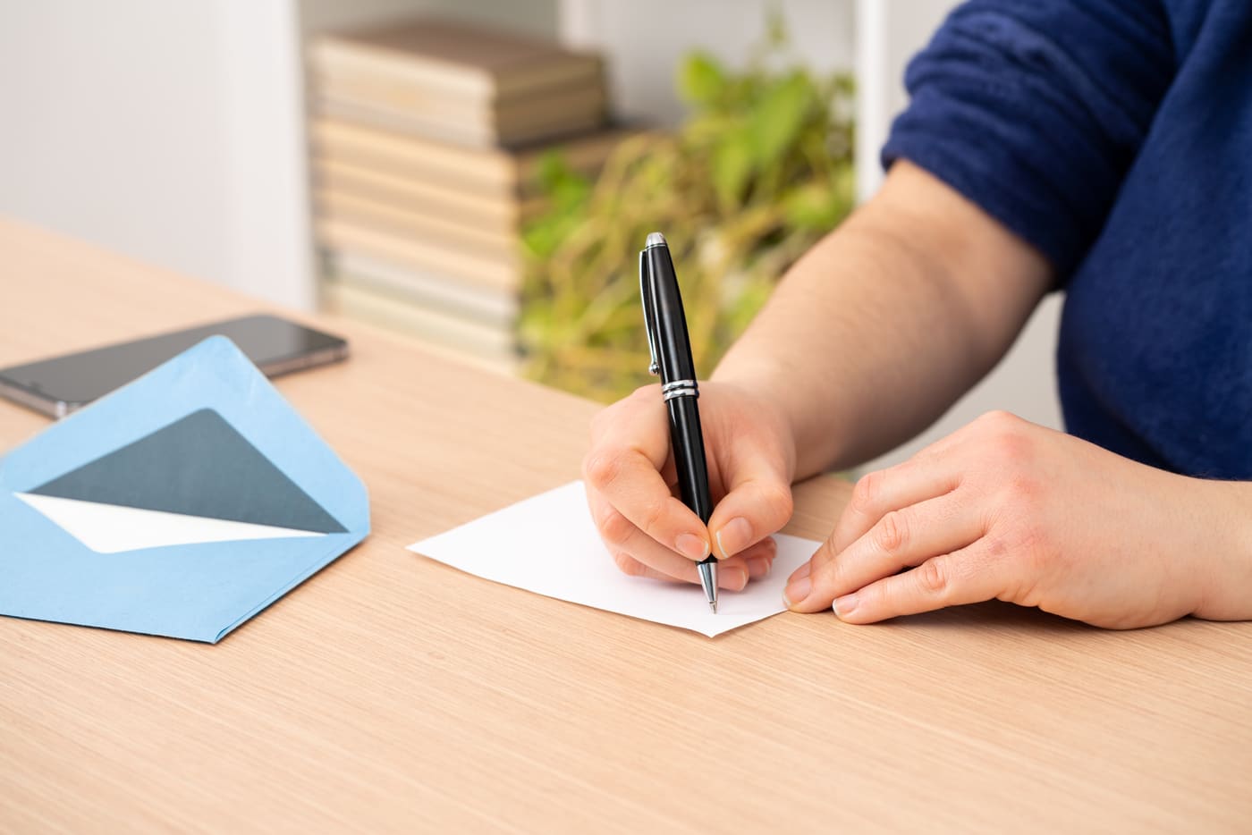A sales rep at a desk writing a handwritten note on a small card, a notebook of call notes open beside it
