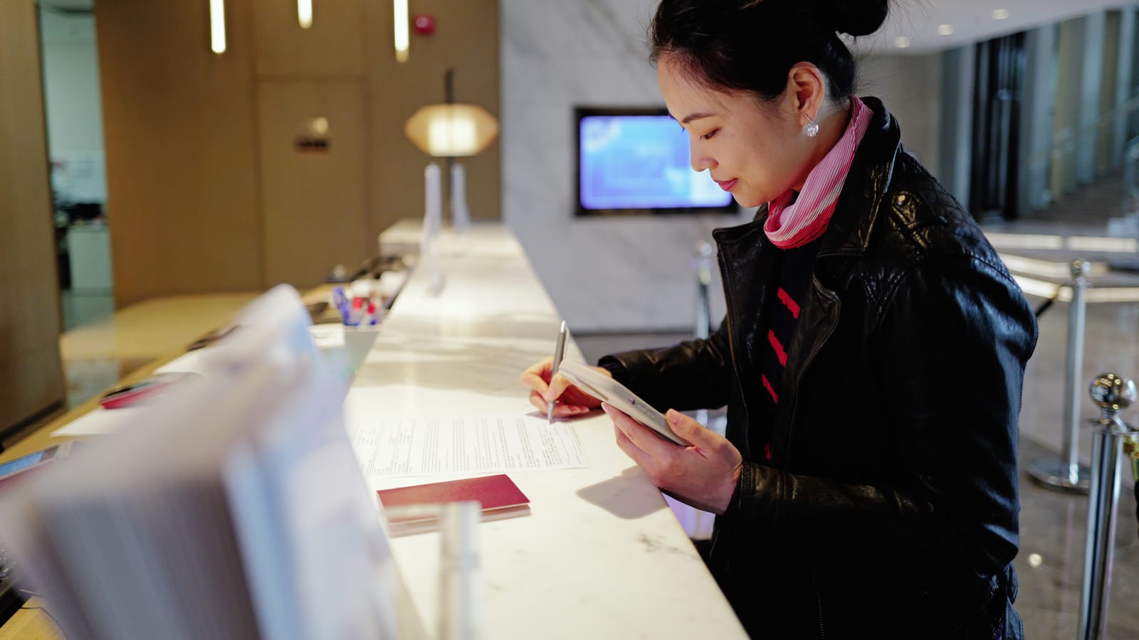 A hotel front desk manager writing a welcome note by hand on a small card, a room key folder beside it on the counter