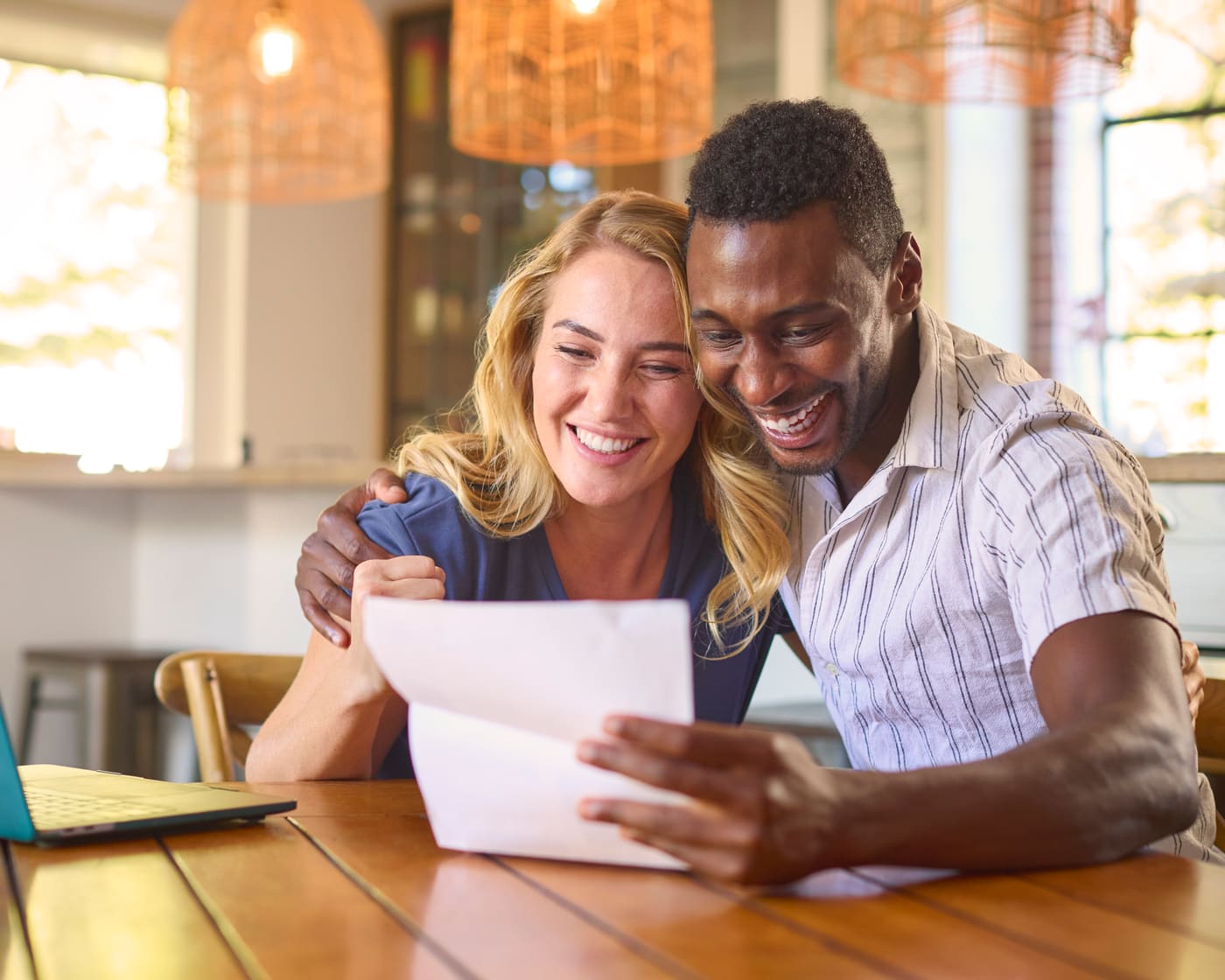 A couple at their kitchen table reading a handwritten thank-you card from their insurance agent, envelope by the mugs