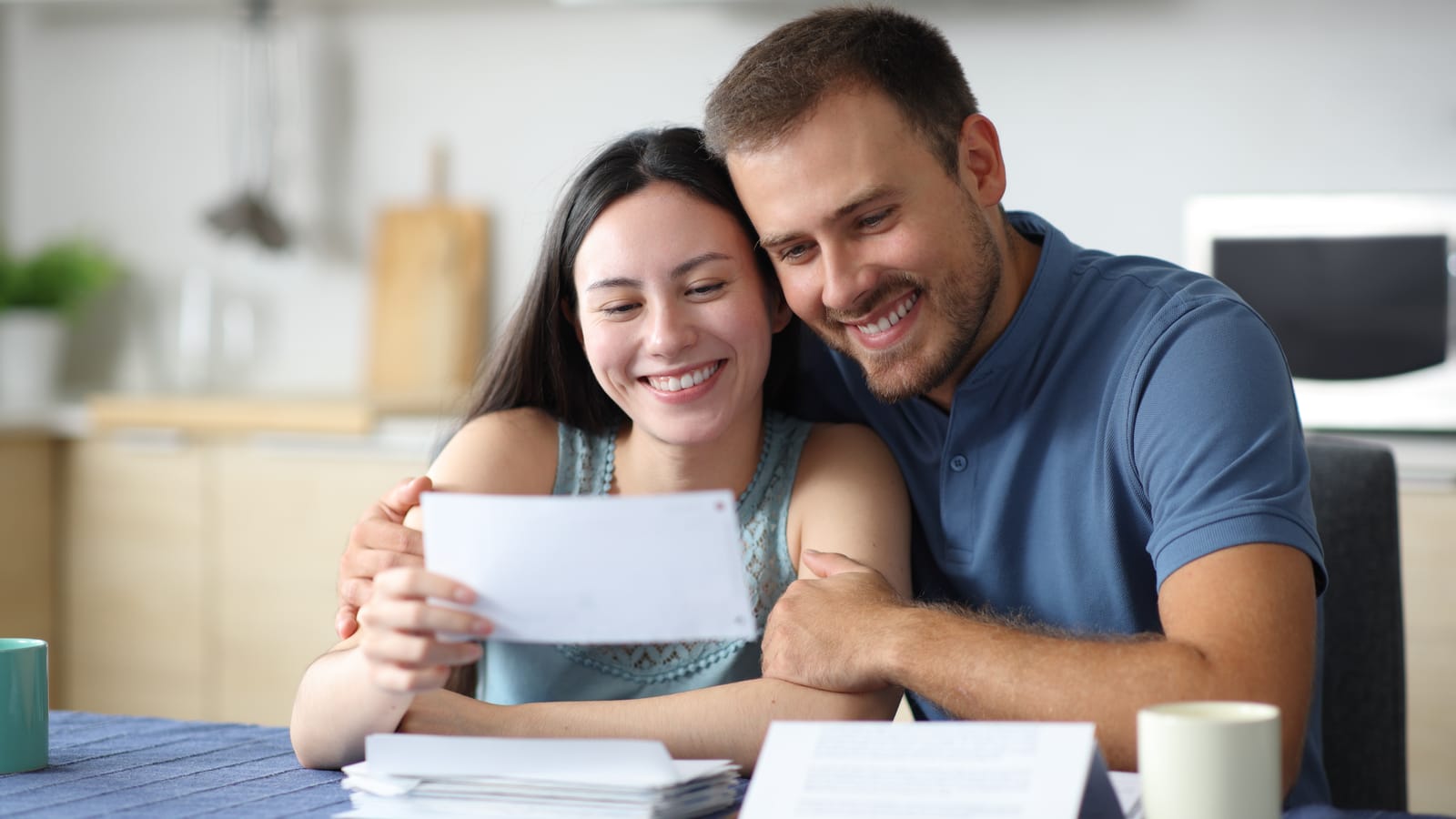 An insurance agent at her office desk writing a thank-you card by hand, a client folder open beside the envelope