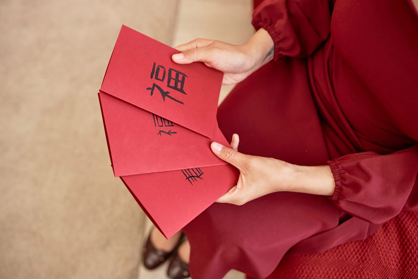 Hands holding three red New Year cards, each brushed by hand with a large character