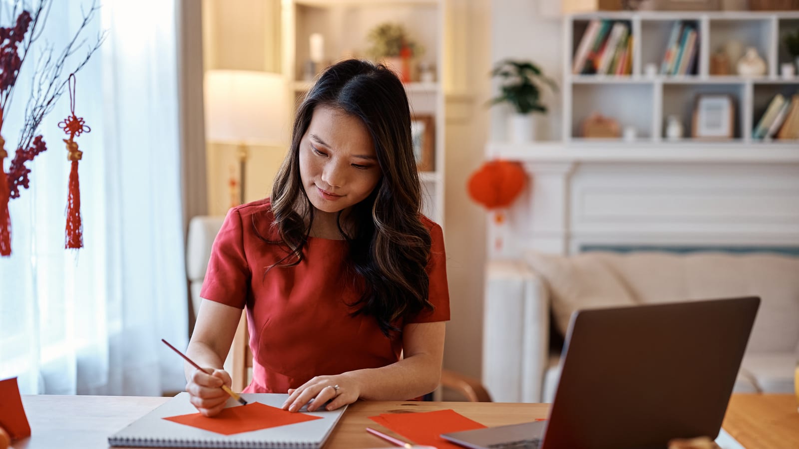 A woman at a desk with her laptop writing a New Year message by hand on red paper