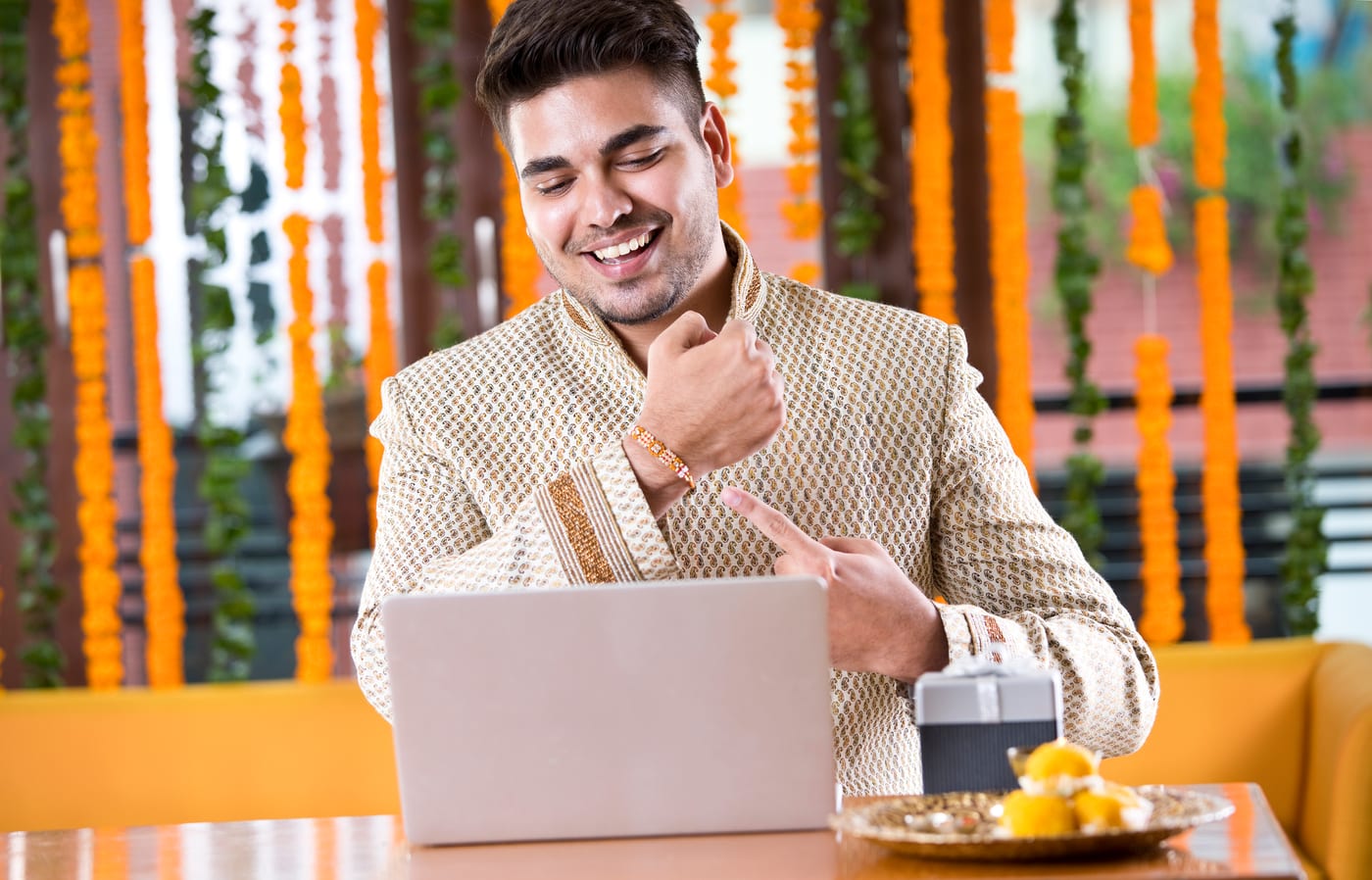 A smiling young man showing the rakhi on his wrist to his sister on a laptop video call