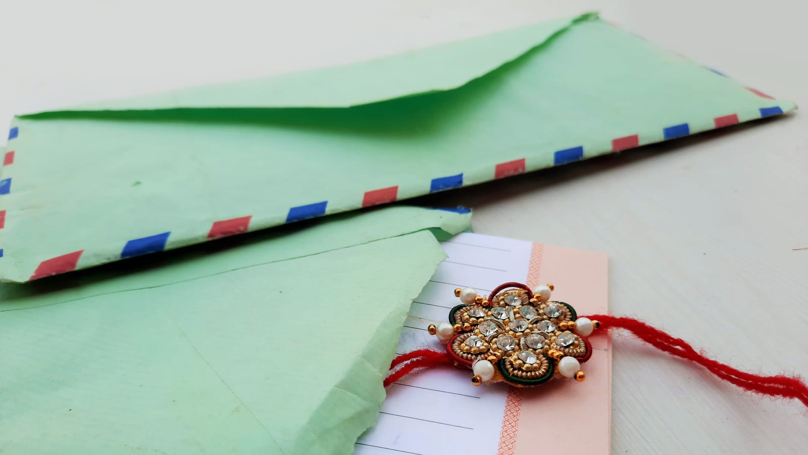 A jewelled rakhi tied around a handwritten note on lined paper, tucked into a green airmail envelope