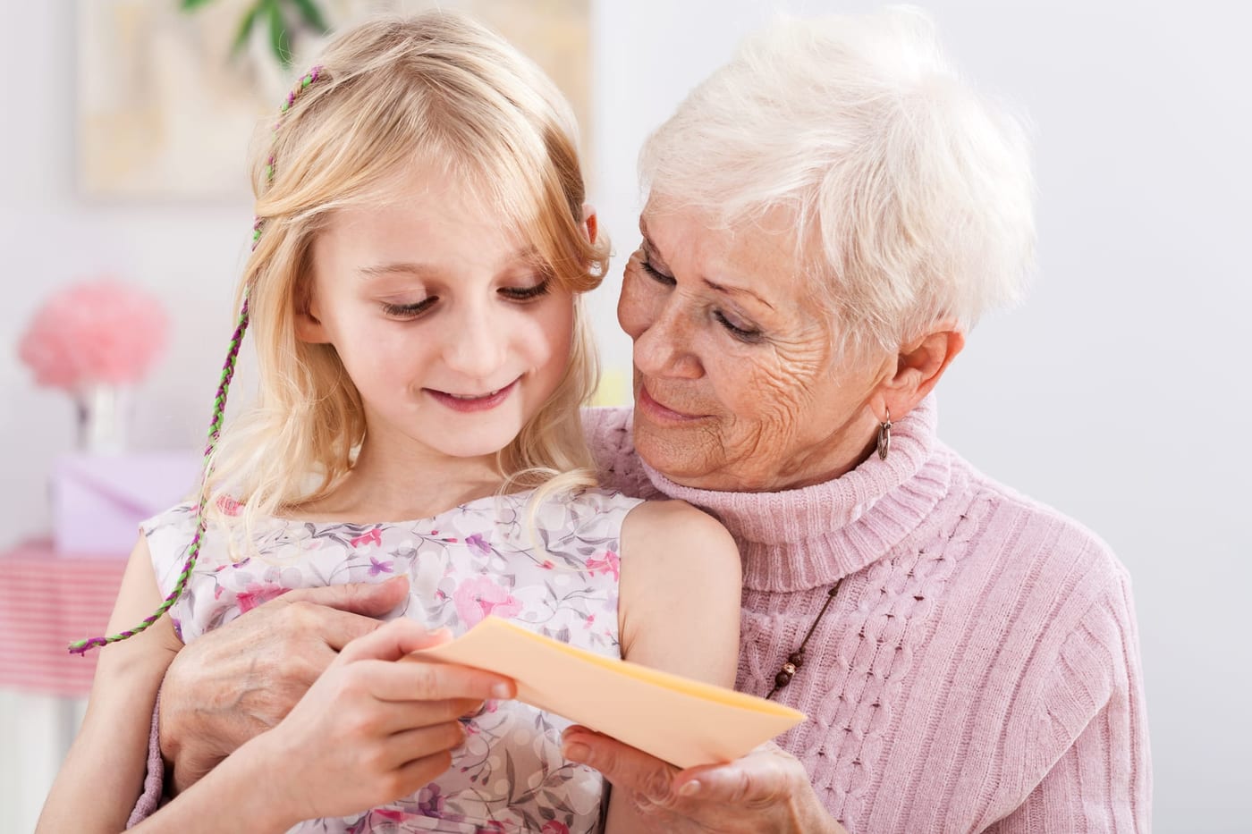 A grandmother sitting at her kitchen table, smiling as she reads a handwritten card she has just opened