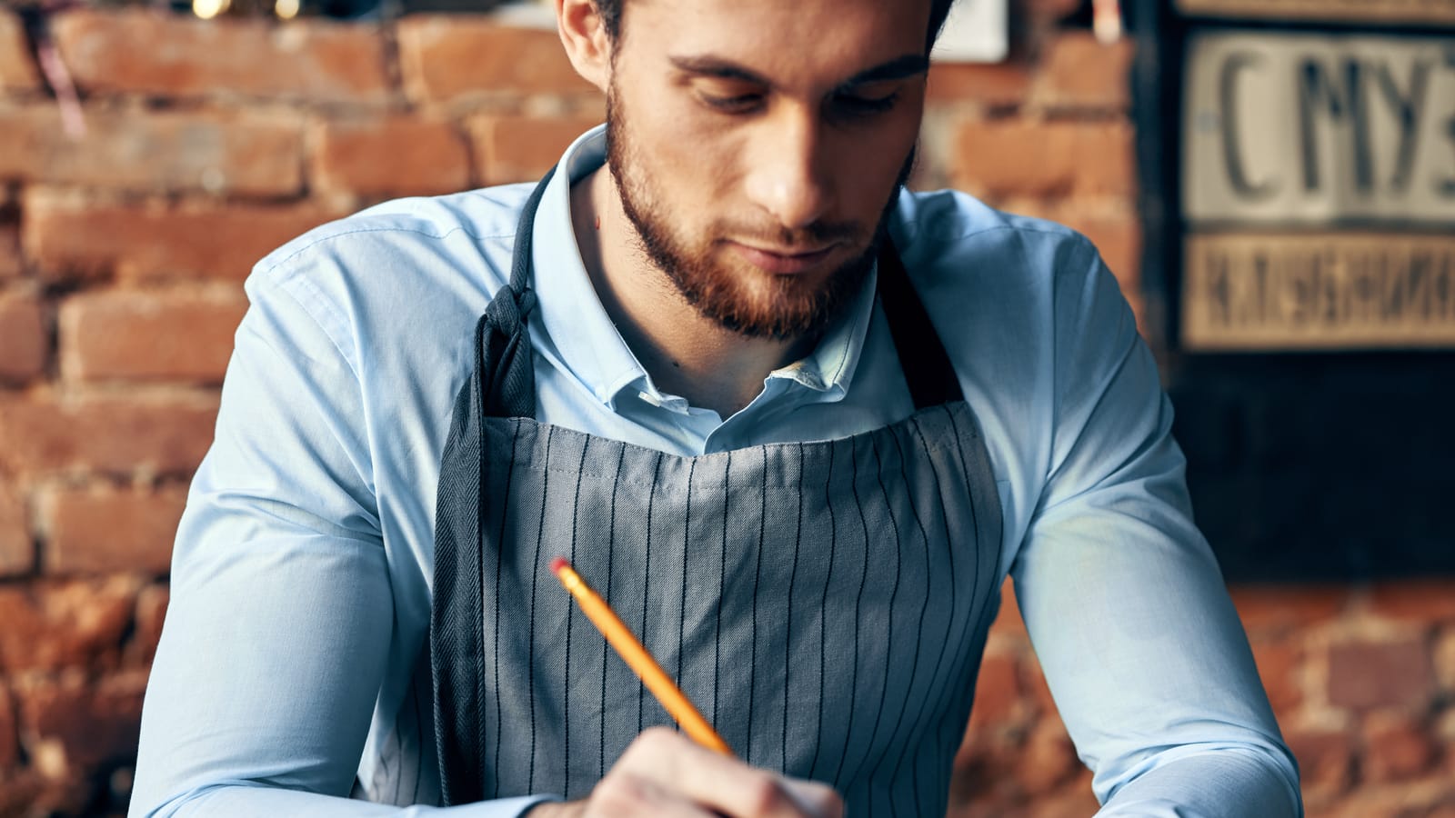 A café owner at the end of the counter writing a thank-you card by hand, a cup of coffee cooling beside the card