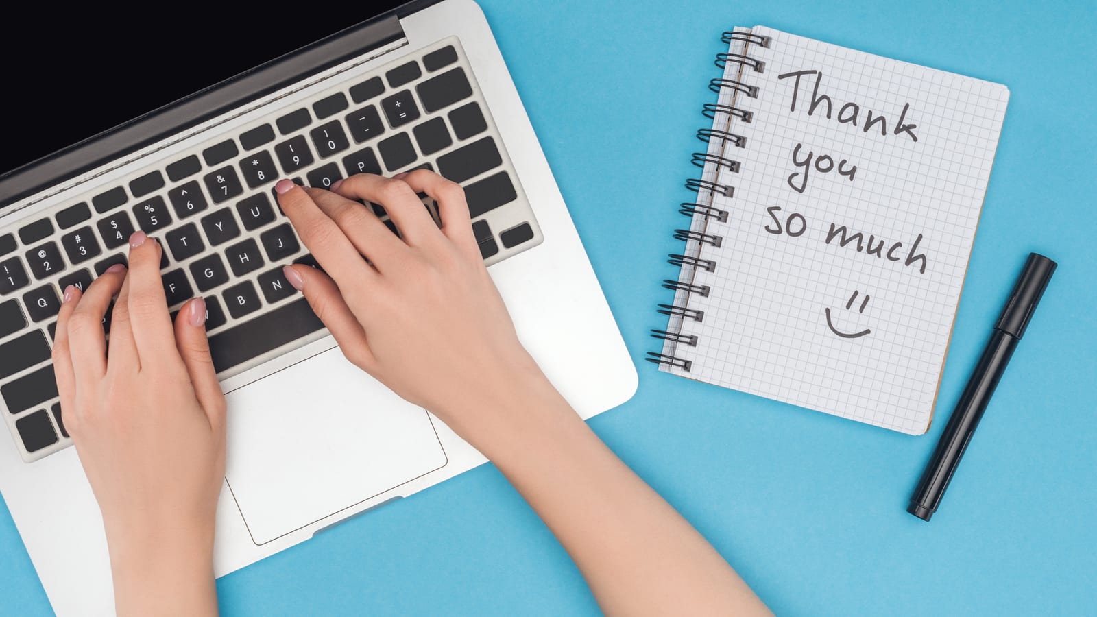 Hands typing on a laptop beside a notebook with Thank you so much written by hand