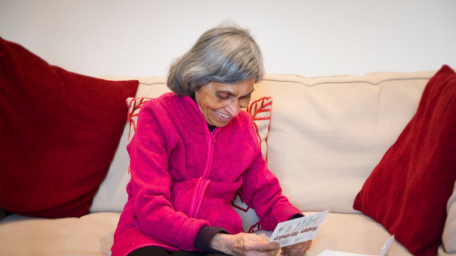 An Indian grandmother on her sofa smiling as she reads a card she has just opened