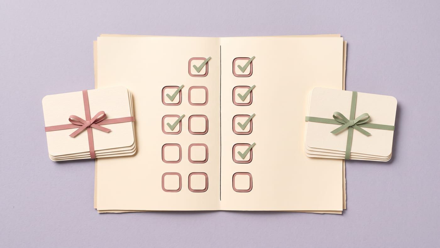 Paper-craft guest list split into two columns of boxes, some ticked, with a ribboned stack of cards beside each column